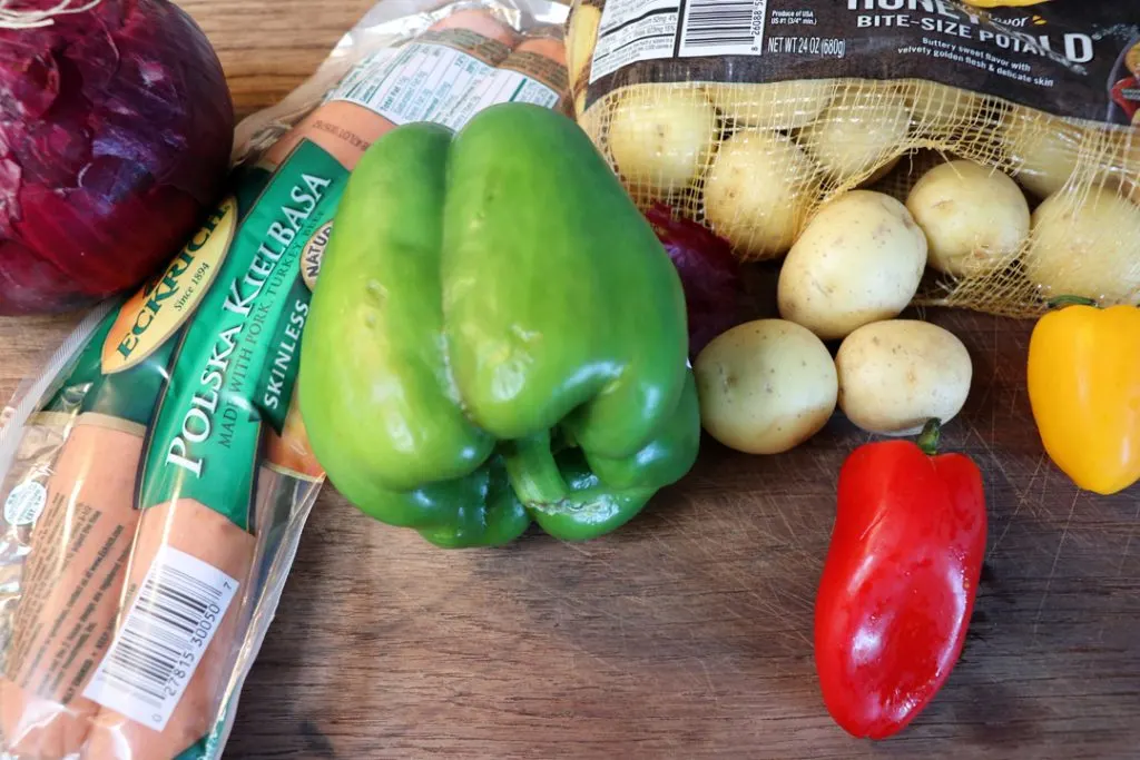 kielbasa, green pepper, red pepper, button potatoes, yellow pepper on a cutting board