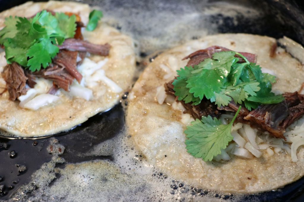 open face birria tacos cooking in cast iron pan