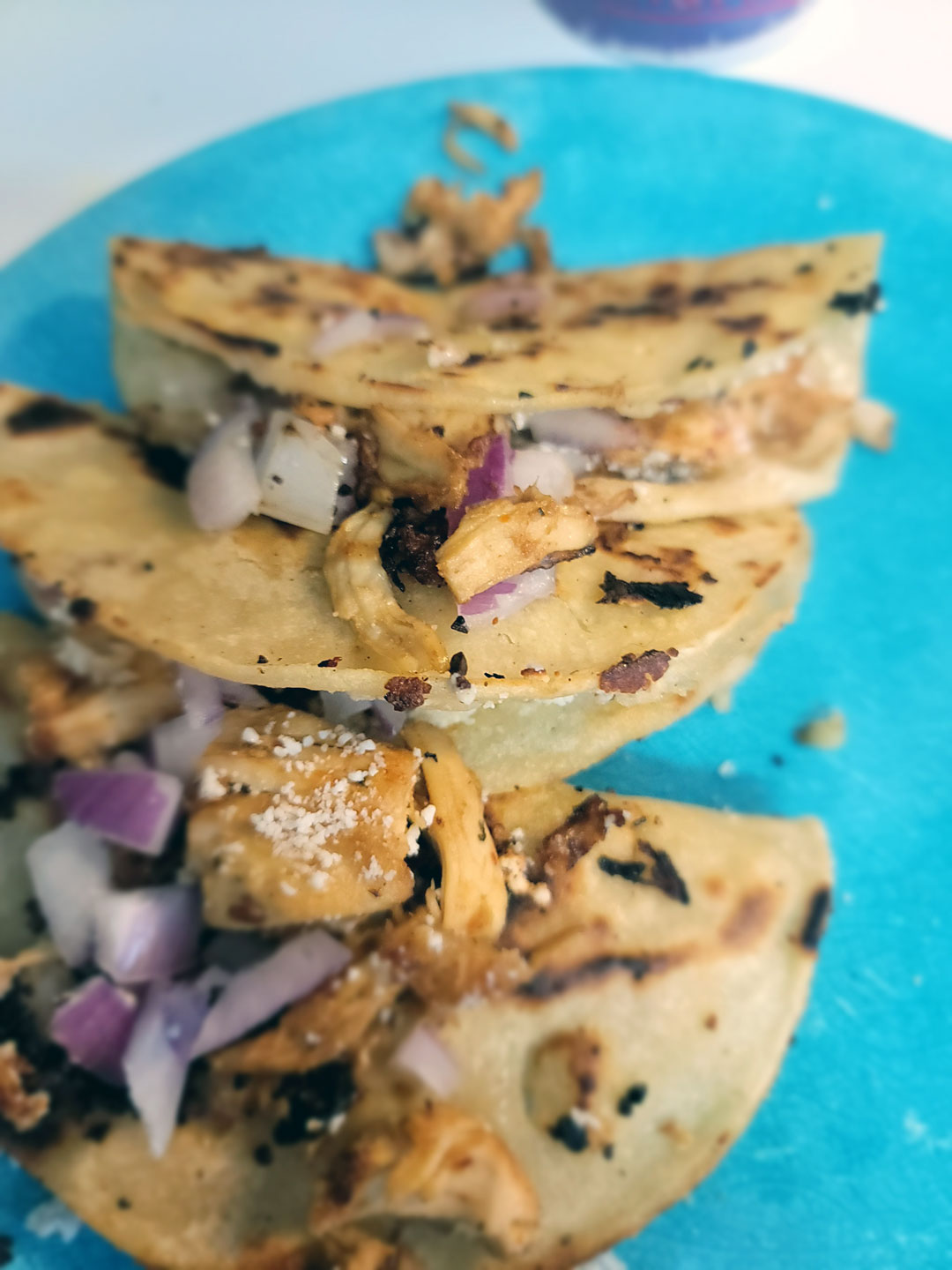 Fried chicken tacos ready to eat on a blue plate with red onions and a corn tortilla