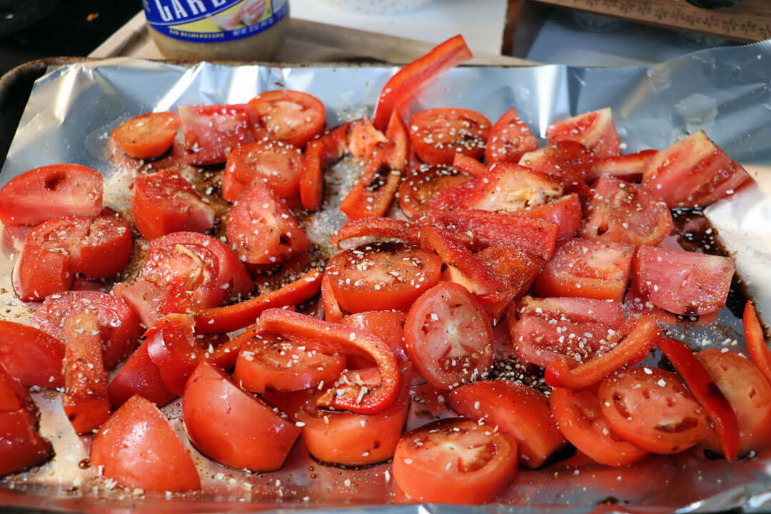 Raw tomatoes and a red pepper on a pan with balsamic and garlic for roasted tomatoes 