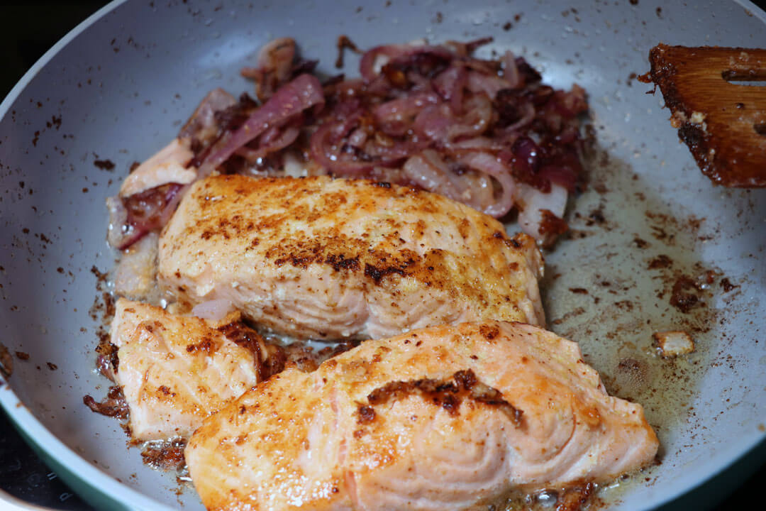 pan-fried salmon in a ceramic pan with cooked red onions