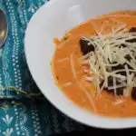 Roasted creamy tomato basil soup in a white bowl with parm cheese and croutons