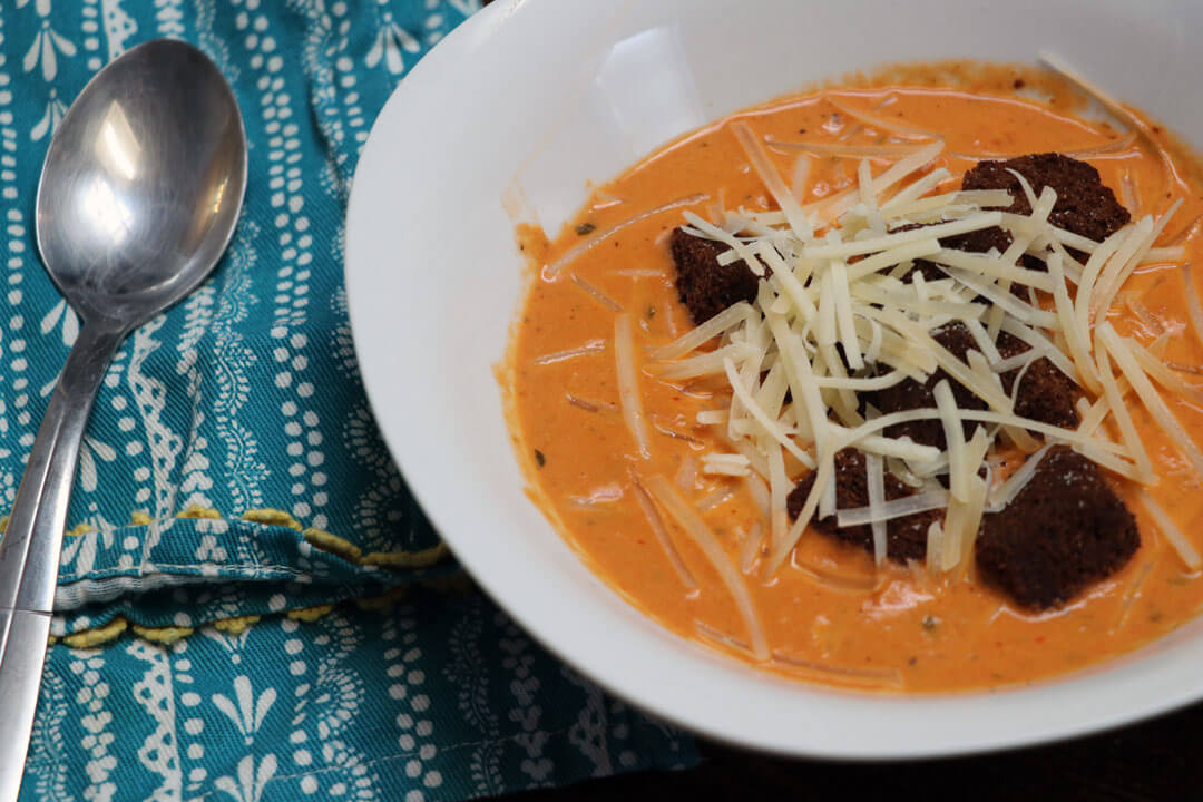 Roasted creamy tomato basil soup in a white bowl with parm cheese and croutons