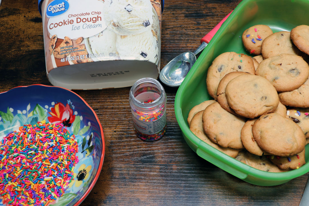 ingredients to make cookie ice cream sandwiches sitting on a table. cookies, ice cream and sprinkles