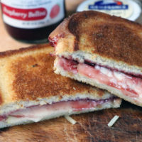 Brie and apple grilled cheese with raspberry jam, cut in half on a cutting board.