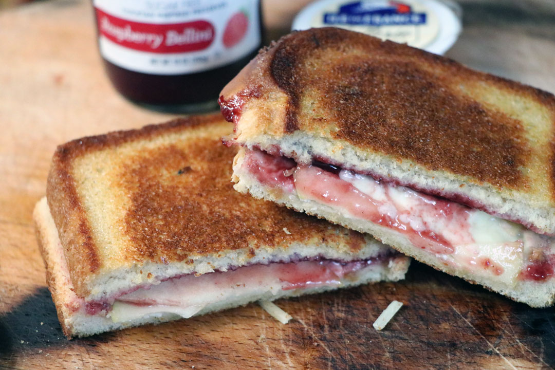 Brie and apple grilled cheese with raspberry jam, cut in half on a cutting board.