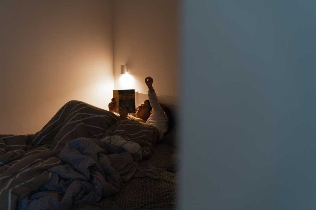 Dim bedroom with soft lighting, person reading in bed