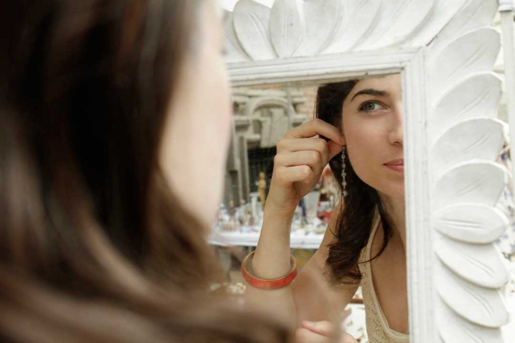 Woman comparing gold and silver earrings in a mirror