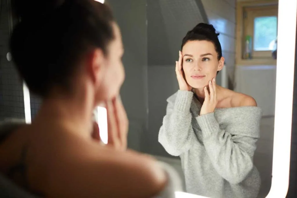 Woman checking her skin for sun damage in bathroom mirror