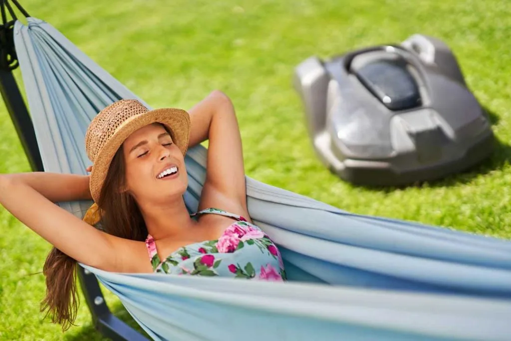 A homeowner relaxing on a patio with a robotic mower working in the background.