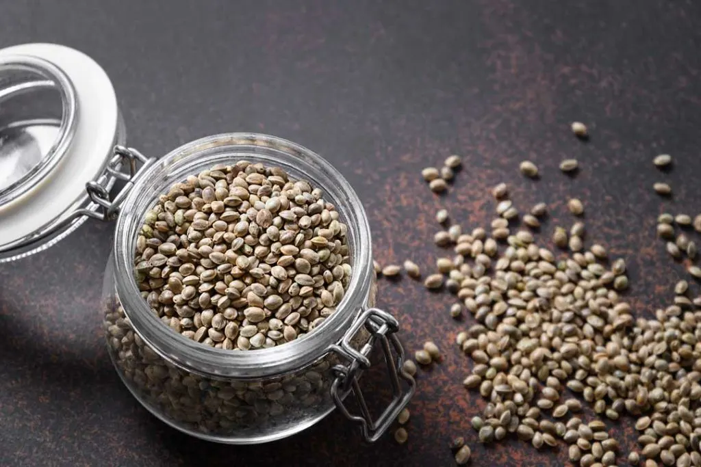 A collection of various cannabis seeds in small, labeled storage containers, illustrating the importance of proper seed storage.