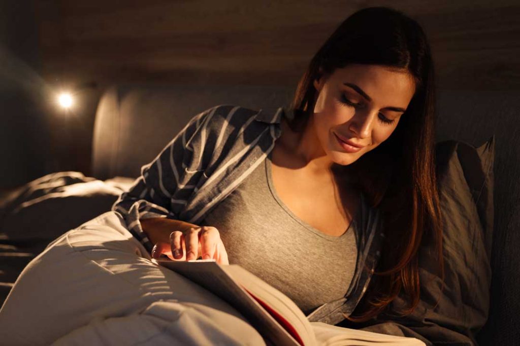 Softly lit bedroom scene with a person reading a book in bed and a diffuser emitting aromatherapy, highlighting elements of a calming nighttime ritual