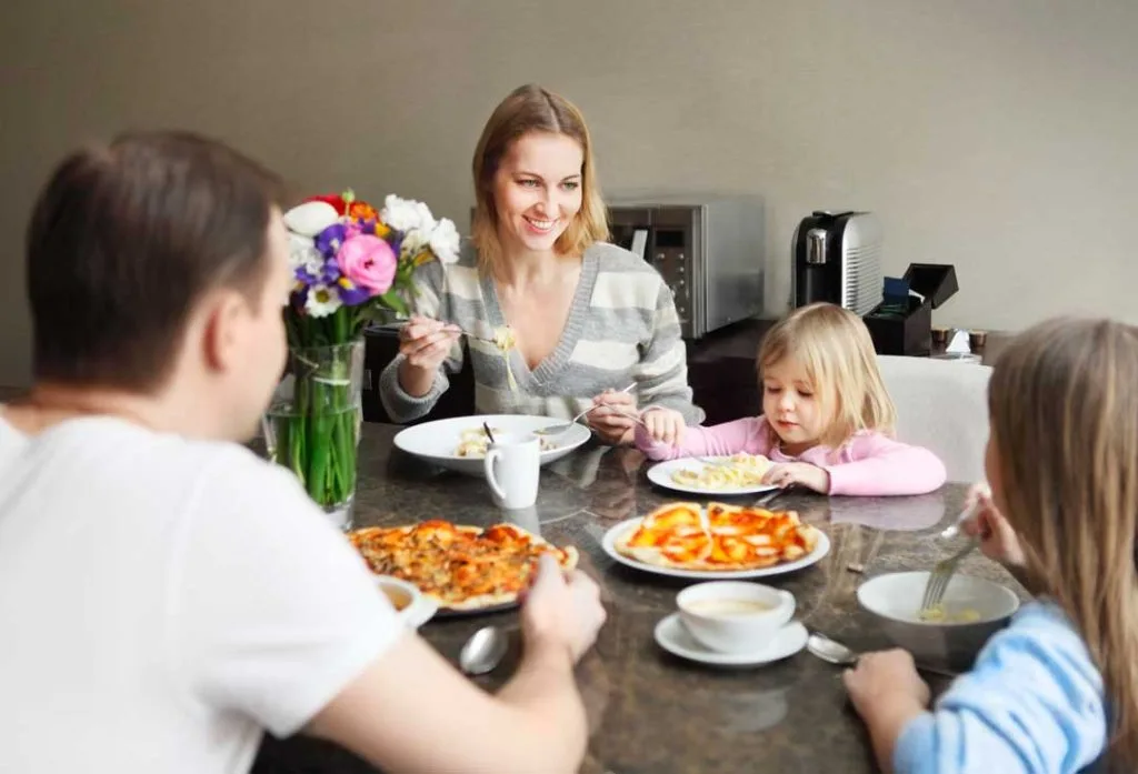 A family enjoying a meal together at a table, with a focus on them eating slowly and engaging in conversation, highlighting mindful family mealtimes.