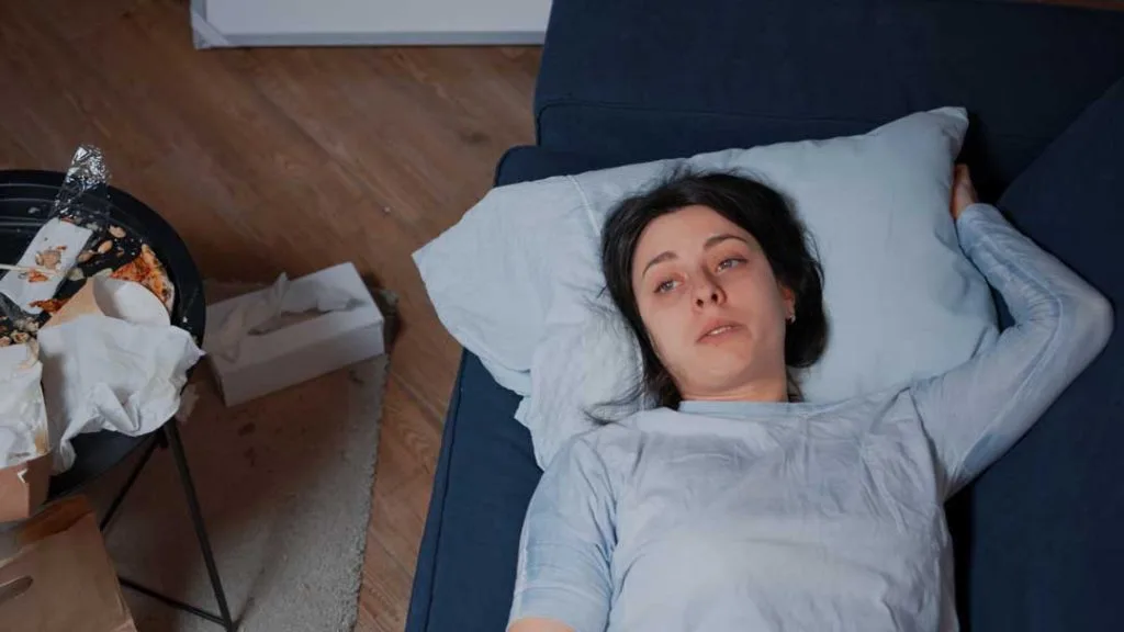 A person lying awake in bed, looking up at the ceiling with a frustrated expression, illustrating the common struggle with insomnia