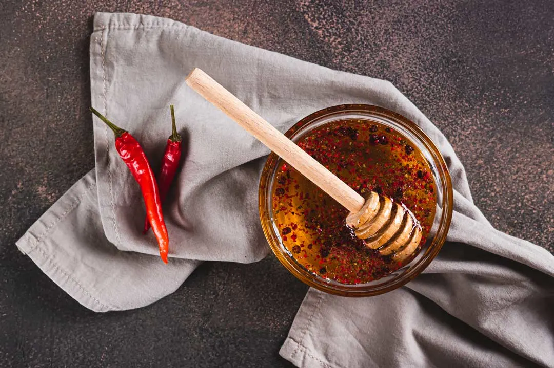 Hot honey sauce bottle with chili peppers and honey dipper